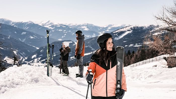 Three people with ski gear on a snowy mountain with a fence and distant snowy peaks.
