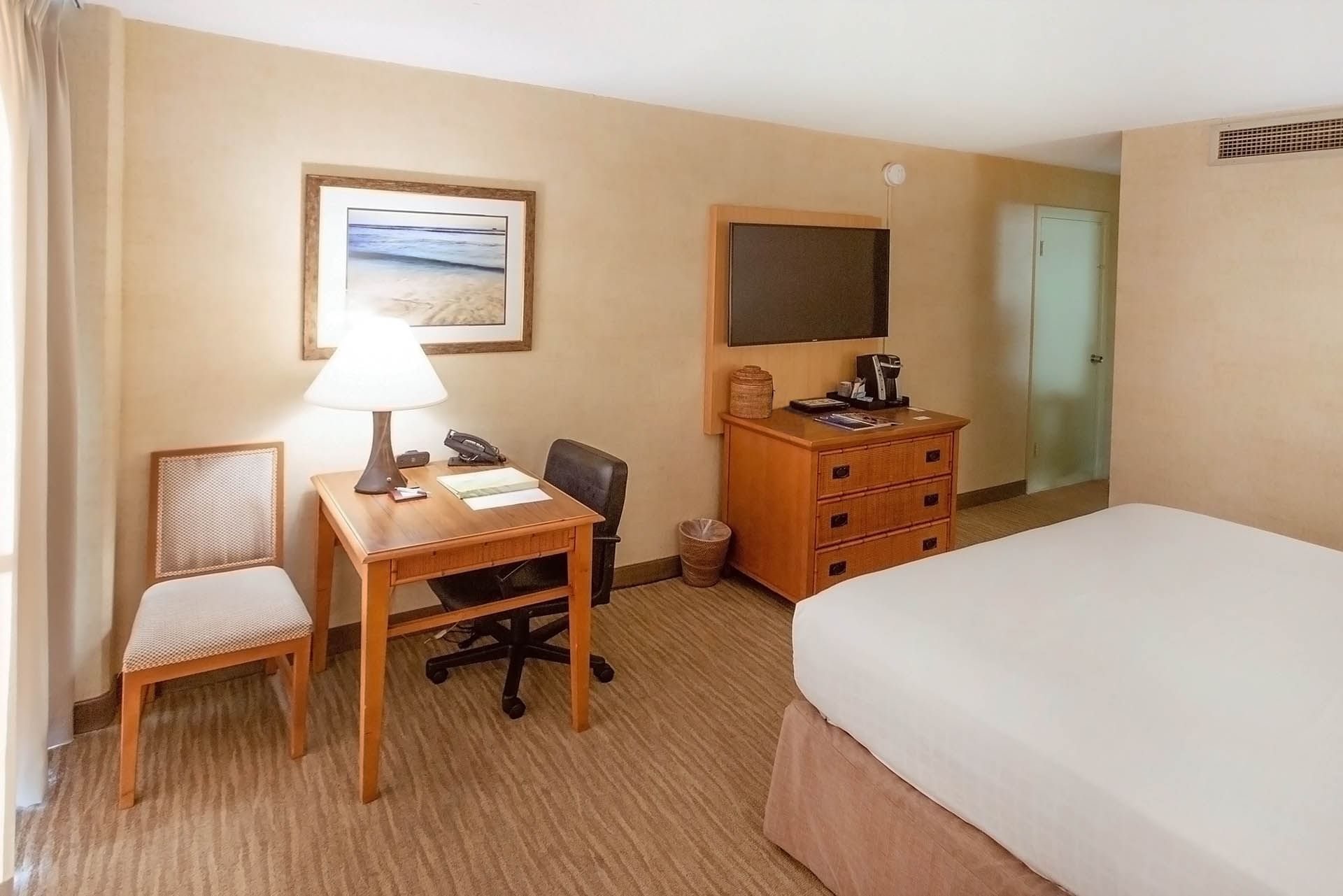 A hotel room with a bed, desk, chair, and TV.