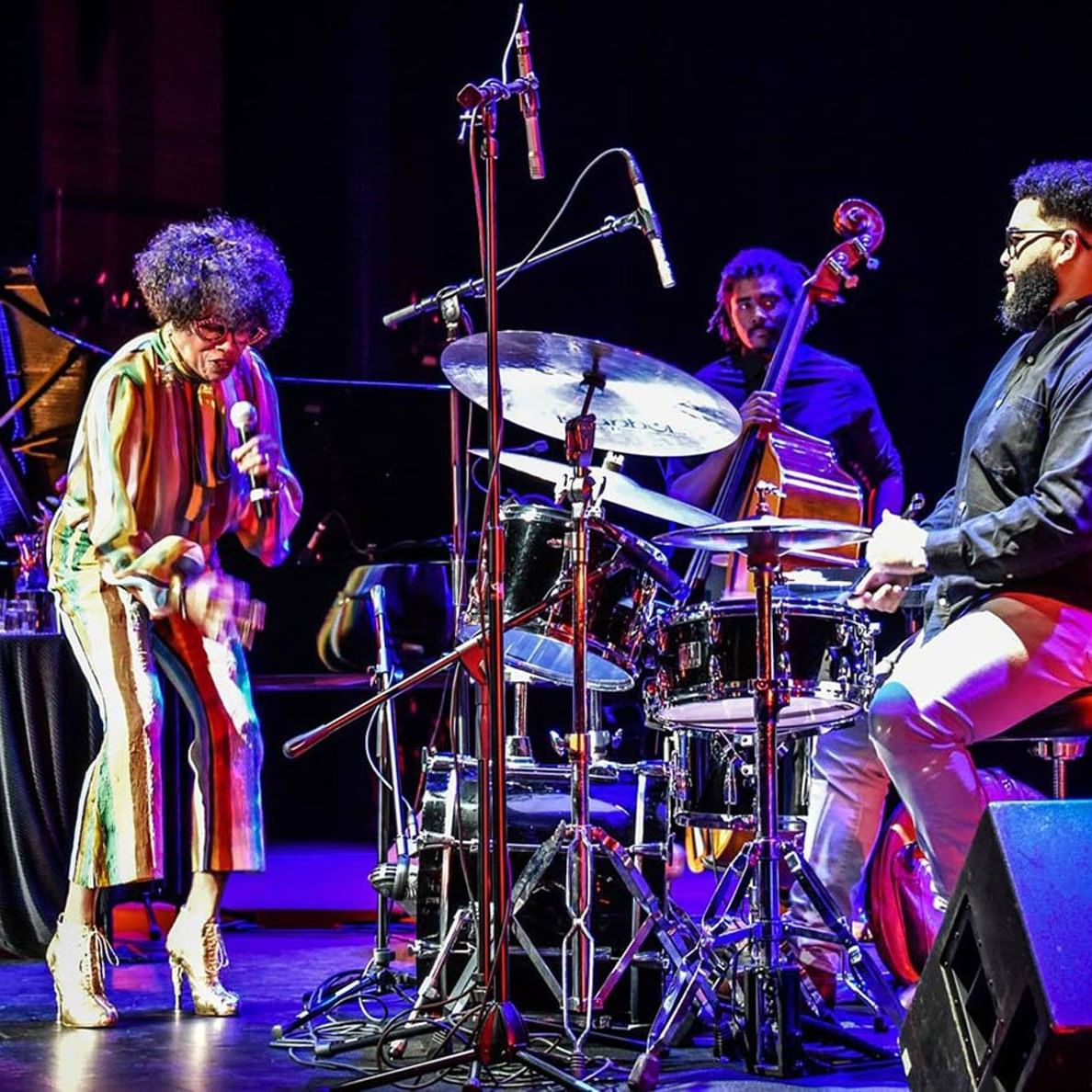 Female jazz vocalist performing lively on stage with a drummer and bassist at an event near Tradewinds Apartment Hotel