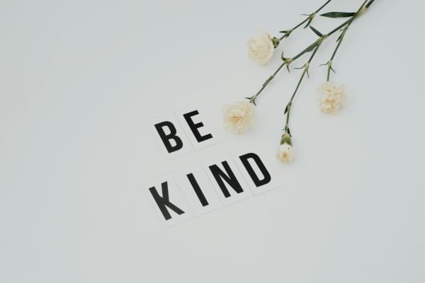 A white backdrop with a sprig of white flowers beside "Be Kind" written in stickers. 