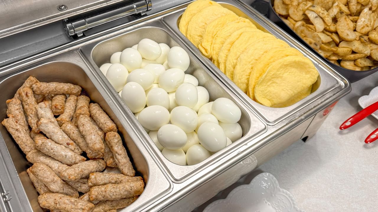 A buffet tray contains sausages, hard-boiled eggs, and yellow scrambled eggs with other food nearby.