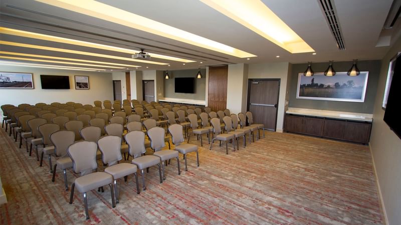Spacious conference room with rows of chairs, lighting, and a projector screen at Fiesta Inn Suites Aeropuerto del Bajío