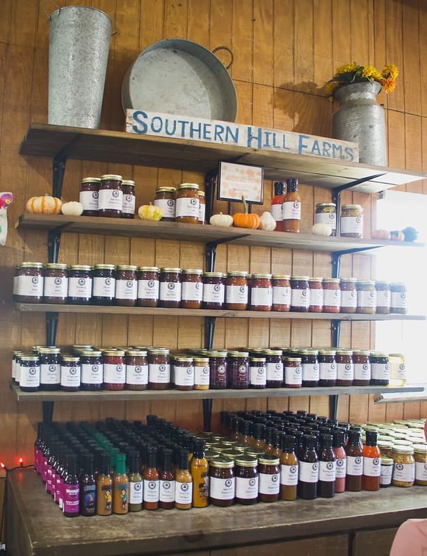 A display of homemade jams and sauces on wooden shelves decorated with tin buckets and a sign that reads "Southern Hill Farms."