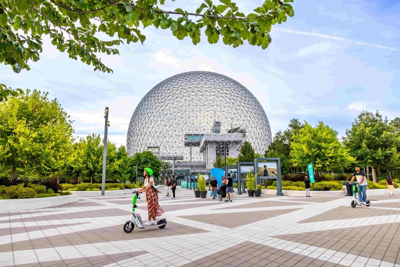 Visitors enjoying the geodesic dome structure surrounded by green trees and pathways at Warwick Le Crystal Montreal