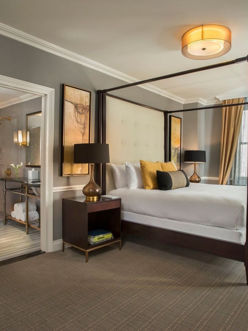 Dark wood four-poster bed between lamps and an en-suite bathroom view in Jane Suite at Warwick New York 