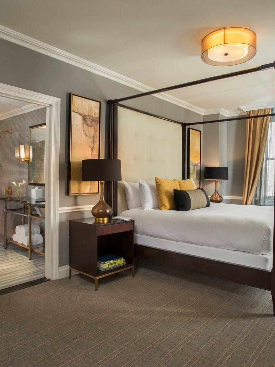 Dark wood four-poster bed between lamps and an en-suite bathroom view in Jane Suite at Warwick New York 