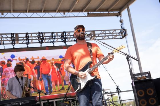 Guitarist in orange playing onstage with sax player in Community Events near Clemson University Conference Center & Inn