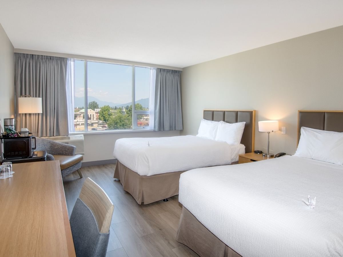 Two beds, nightstands, lamps, and a chair near a window with a mountain view.