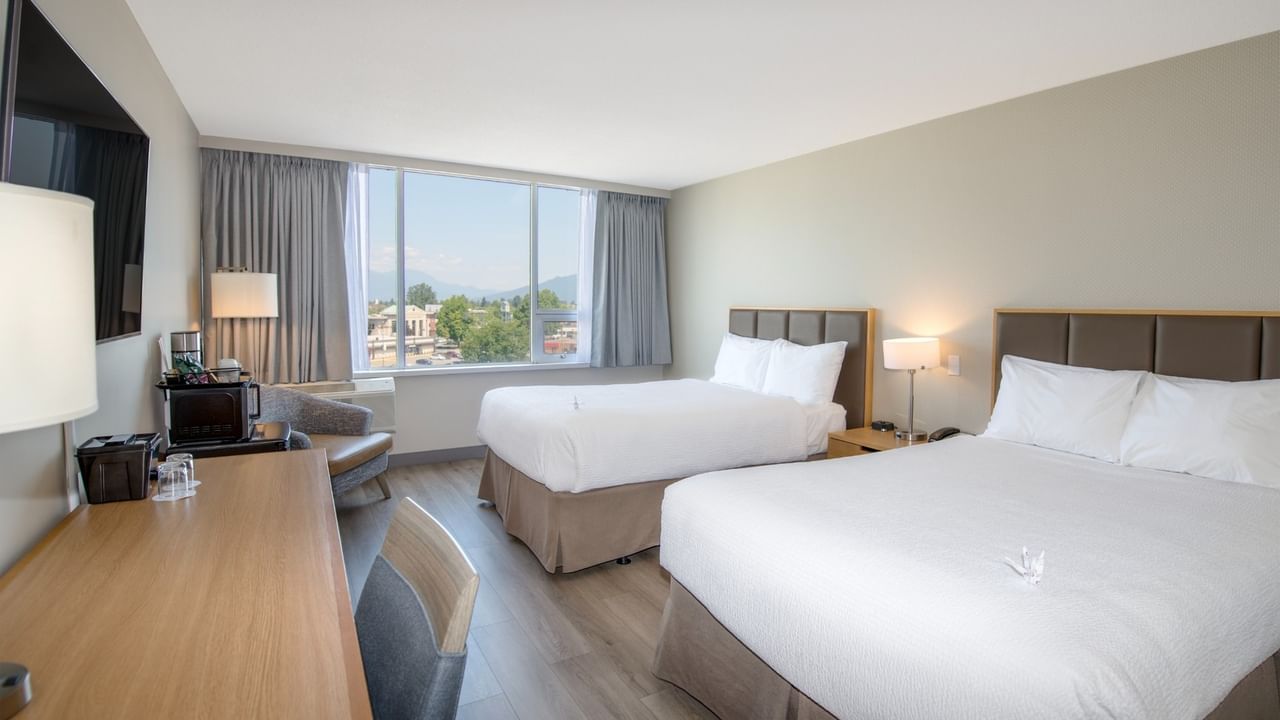 Two beds, nightstands, lamps, and a chair near a window with a mountain view.