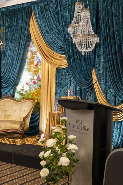 Podium stage setup by a tufted sofa under crystal lamps at Rodd Miramichi River, a premier venue for Miramichi events