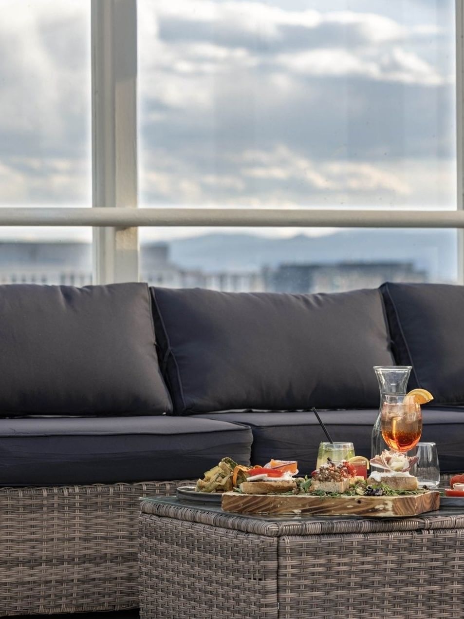 Wicker sofa with dark cushions by a glass table under a cloudy sky in Pool Bar (Seasonal) at Warwick Denver