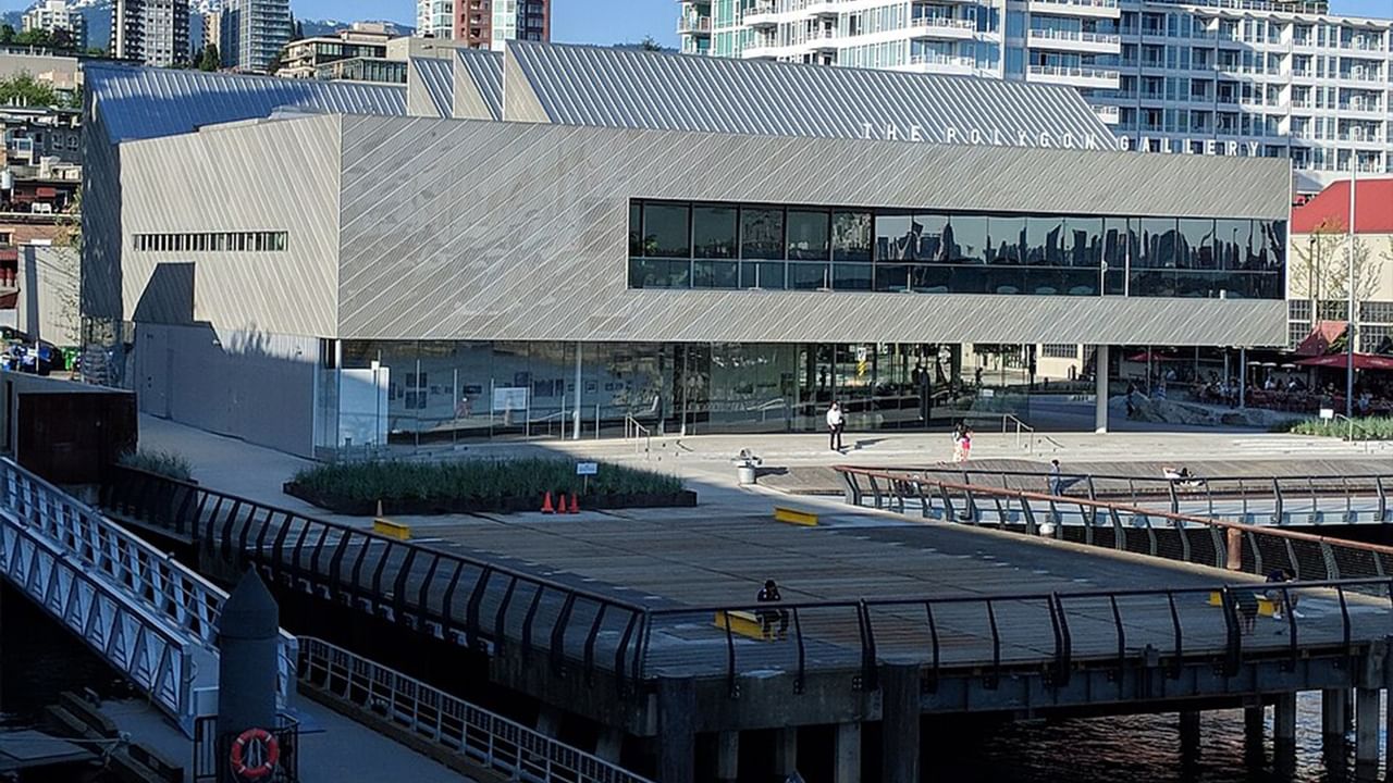 Modern building with glass facade and slanted roof, next to a bridge over water near Coast Lonsdale Quay Hotel 