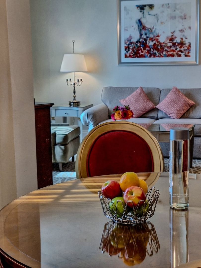 Fruit bowl on a wood table by a grey sofa under floral art in Deluxe Suite Accessible at Warwick Melrose Dallas