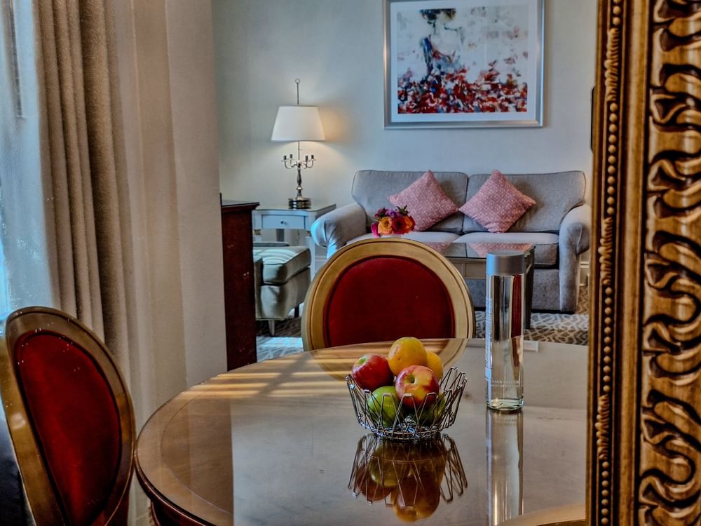 Fruit bowl on a wood table by a grey sofa under floral art in Deluxe Suite at Warwick Melrose Dallas