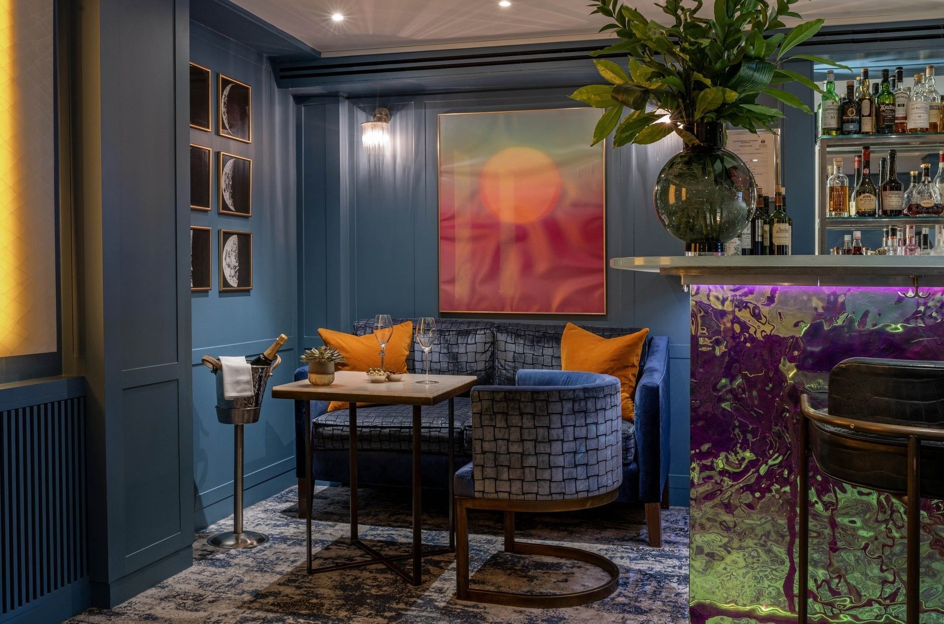 Blue velvet sofa by a table with champagne and a vibrant art piece at The Capital Hotel, Apartments and Townhouse