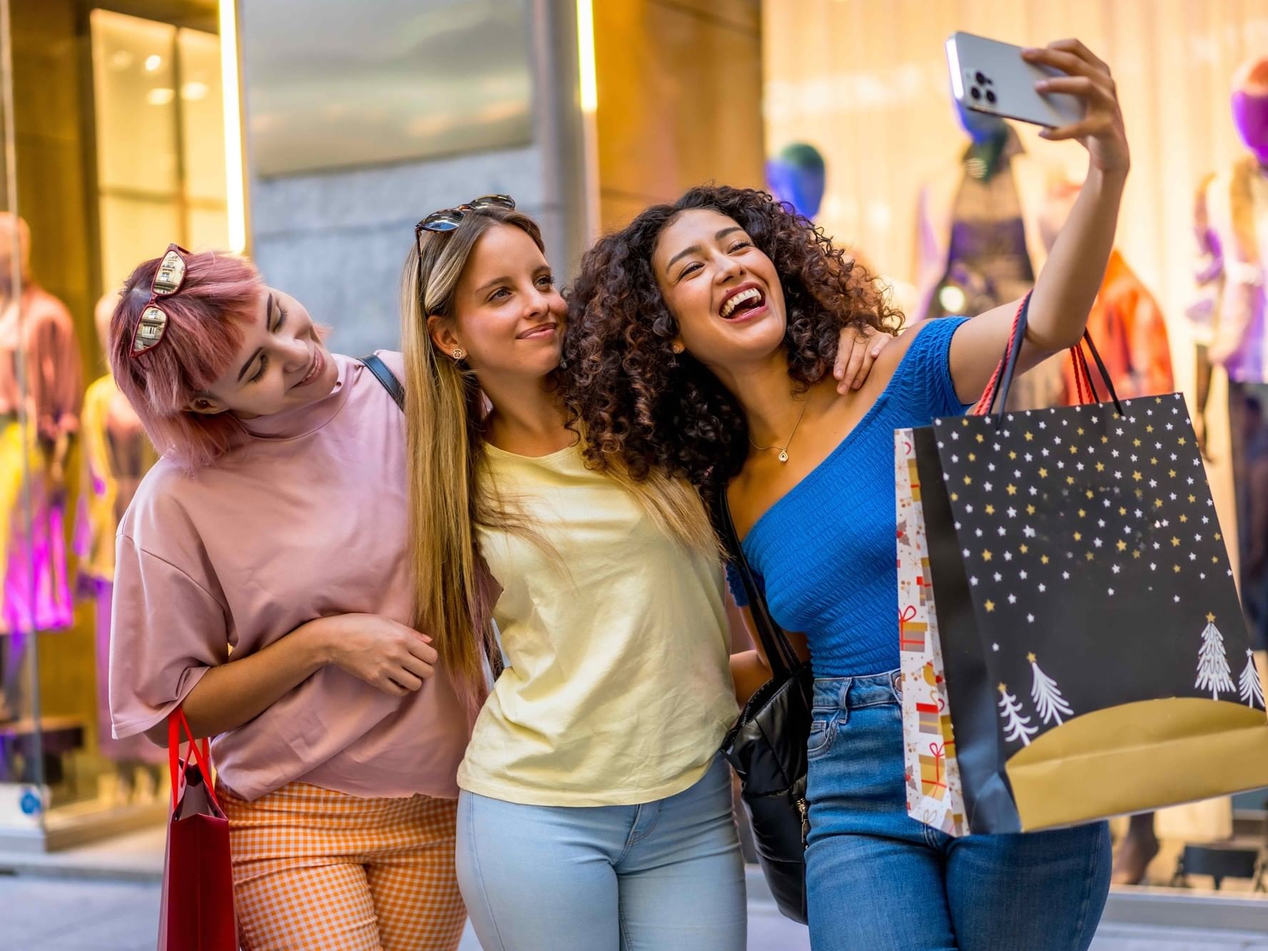 Three women shopping and taking a selfie in front of a store for a Girls' Getaway offer.