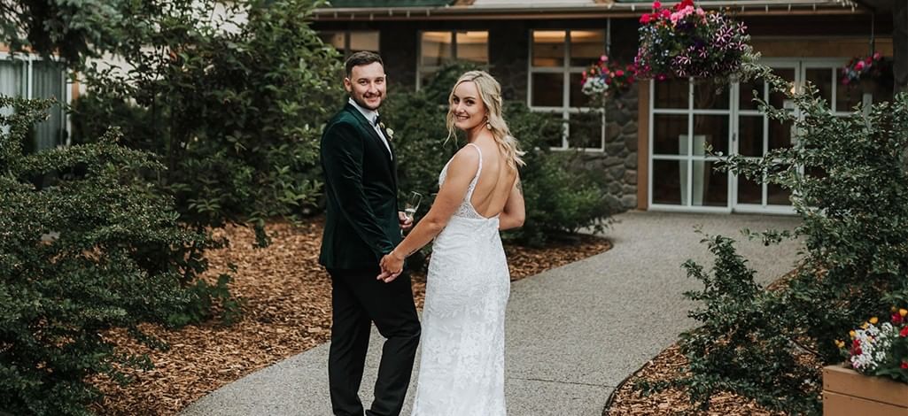 A bride and groom walk towards their micro wedding venue in Canmore and look back at the camera.