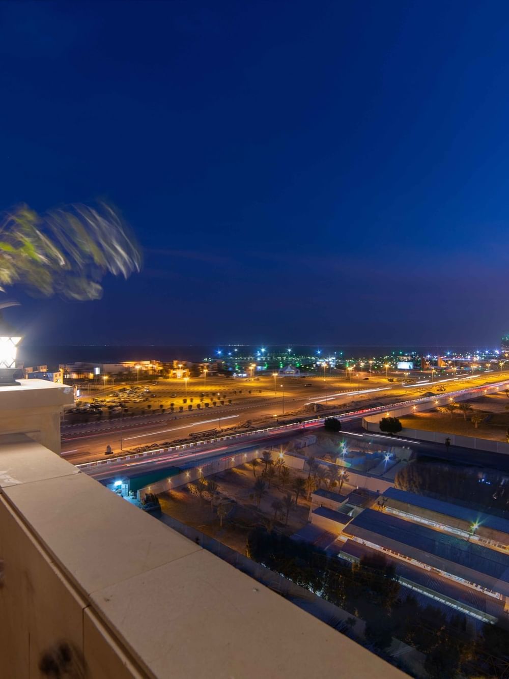 Night city view from a balcony by a potted plant and lamp under a dark sky in Penthouse Villa at Warwick Al Khobar