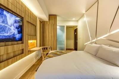 TV, workspace, and stylish wooden furniture by the bed in Corner King Room with geometric wall design at Hotel Nodo
