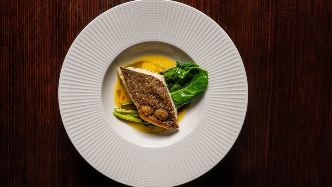 Seared fish fillet with green vegetables and yellow sauce on a white textured plate for NRL Grand Final Dining