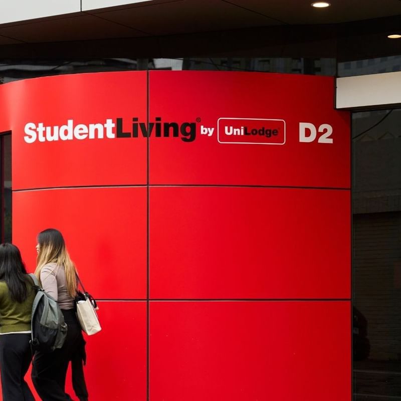 Two residents walking past a red Student Living D2 sign at entrance