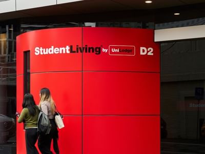 Two residents walking past a red Student Living D2 sign at entrance