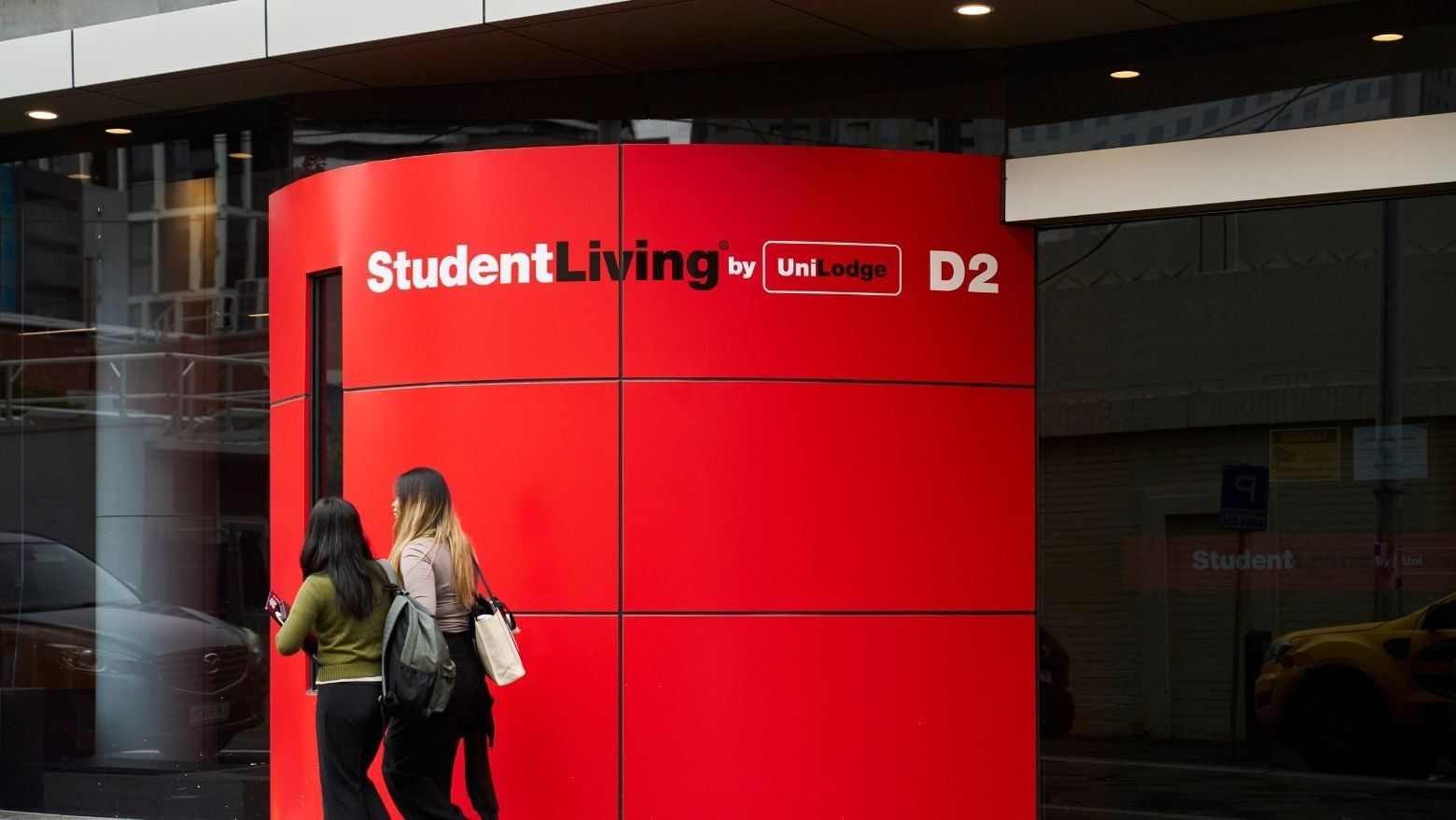 Two residents walking past a red Student Living D2 sign at entrance