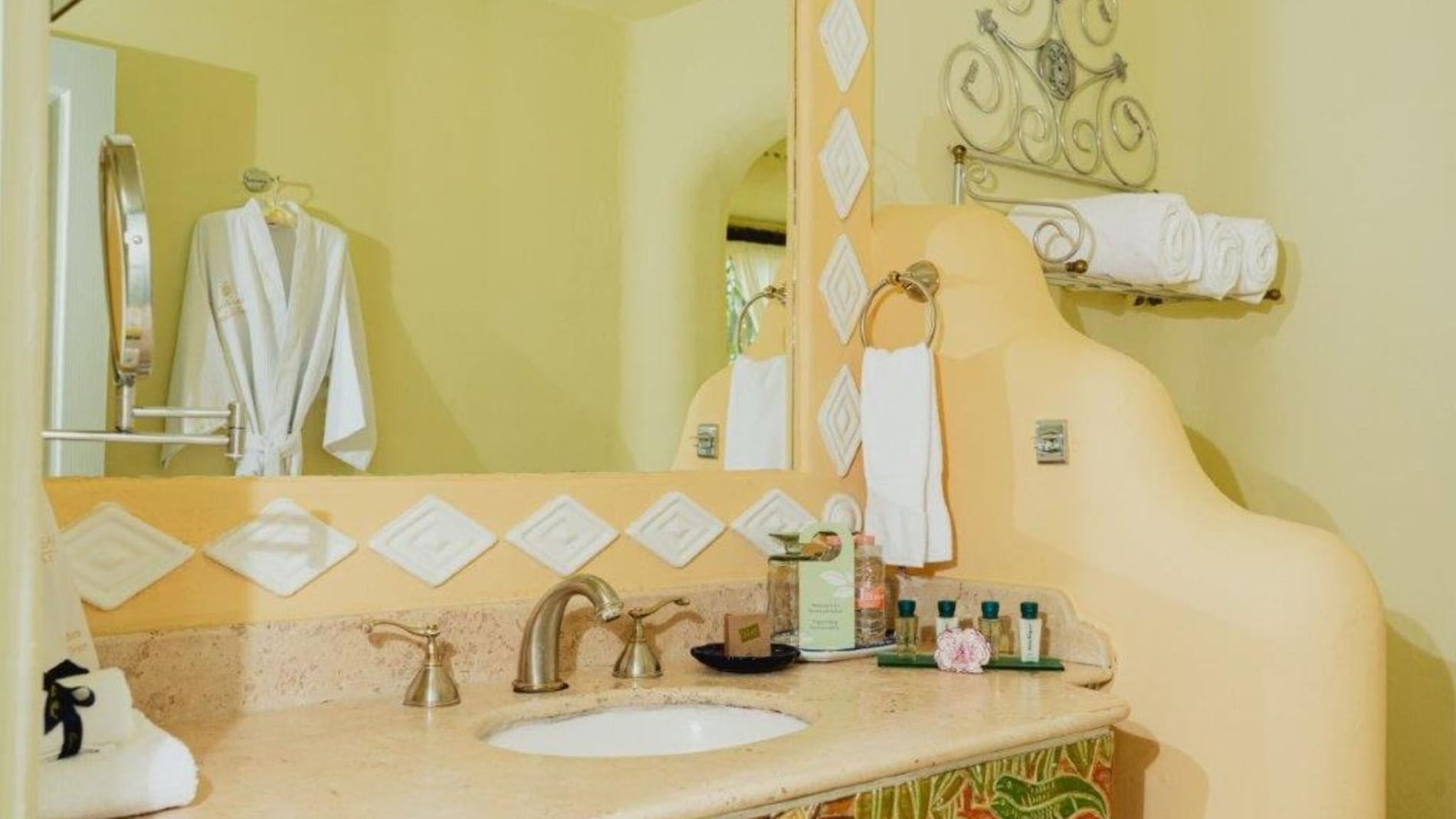 King Master Suite bathroom featuring a carved vanity, large mirror, and plush white bathrobes at Quinta Real Huatulco