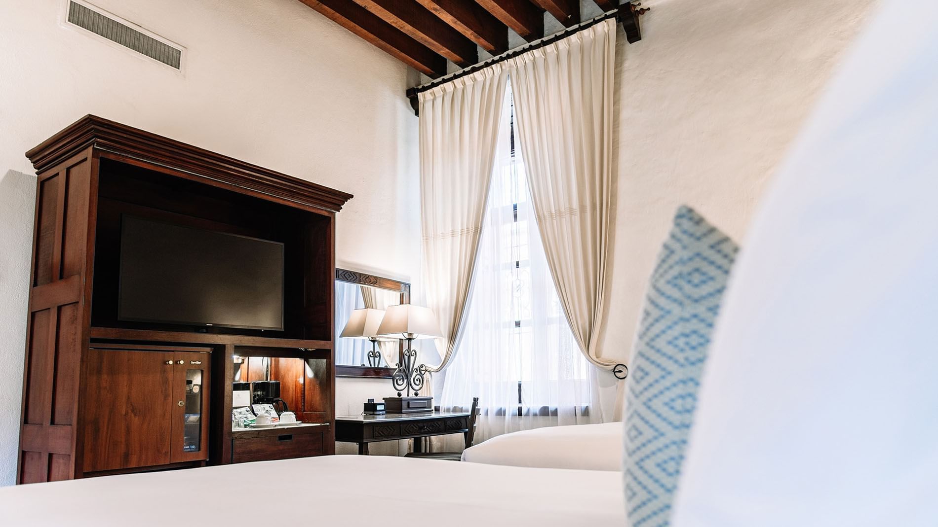 2 Double Superior Suite featuring a TV on a wooden cabinet, a work desk with lamps, and plush bedding at Quinta Real Oaxaca