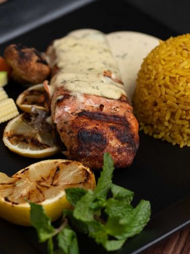 سمك السلمون المشوي مع شرائح الليمون، محاطًا بقبة من الأرز الأصفر والخضروات المطهوة على البخار في مطعم «وارويك» بالجبيل