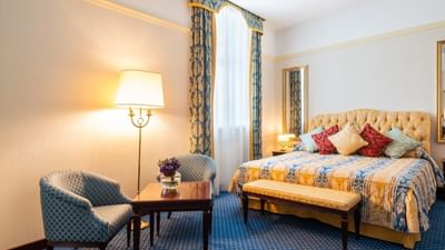 Bedroom with patterned blue curtains, plush bed, and a cozy sitting area at Polonia Palace Hotel