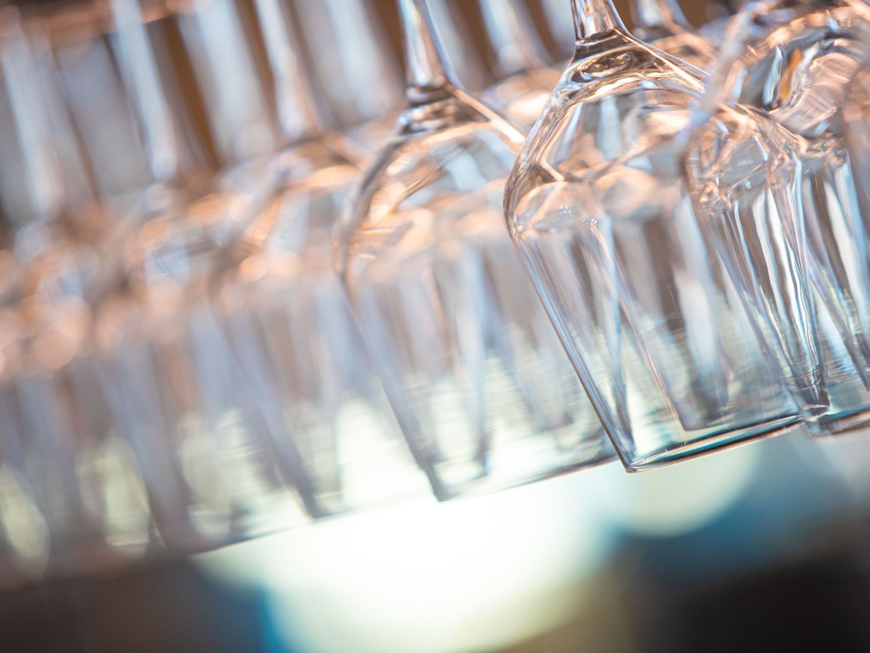Close-up of multiple clean wine glasses inverted and hanging on a professional glass rack.