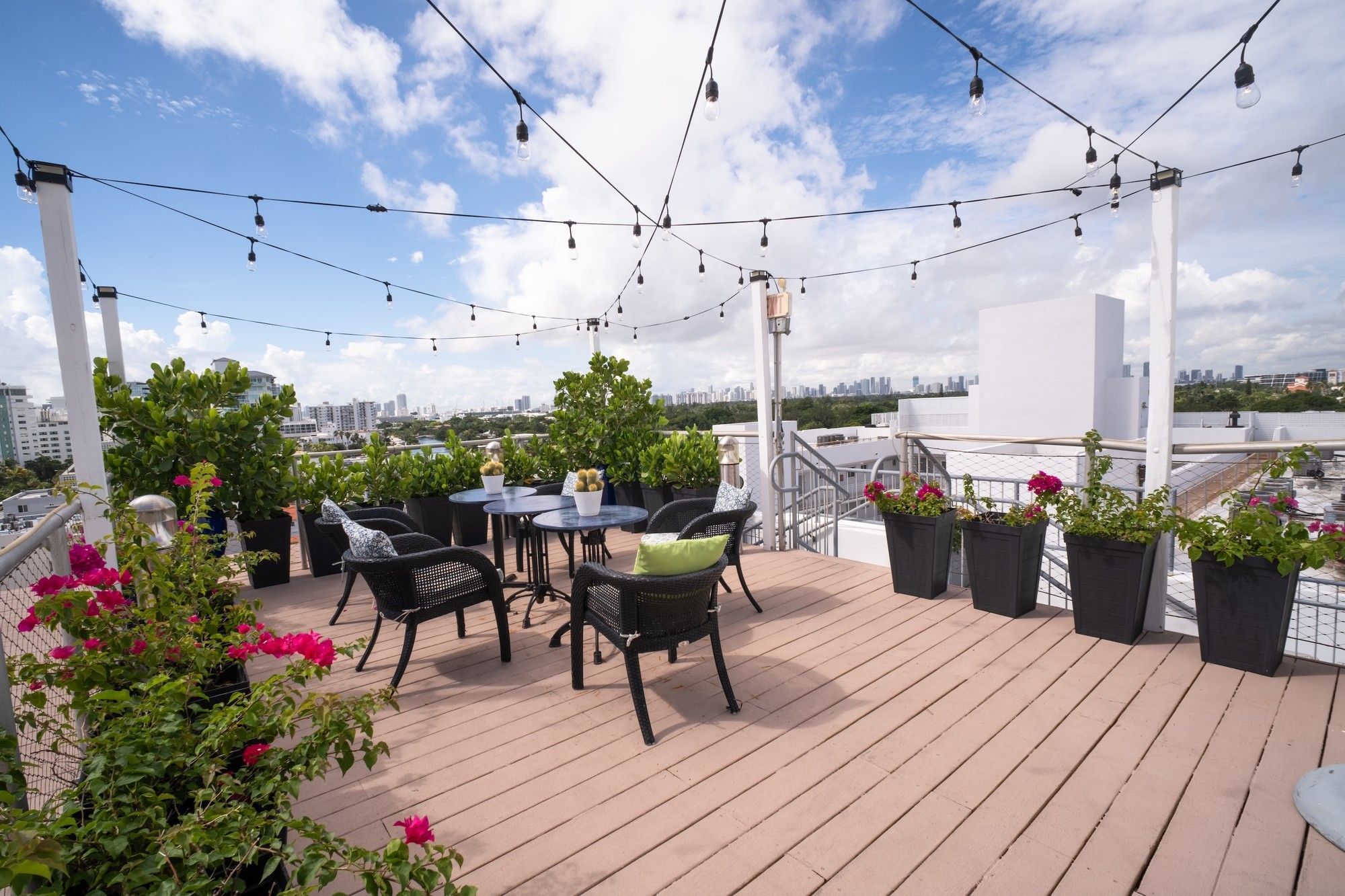 A rooftop deck with outdoor furniture, potted plants, and string lights overlooking the city.