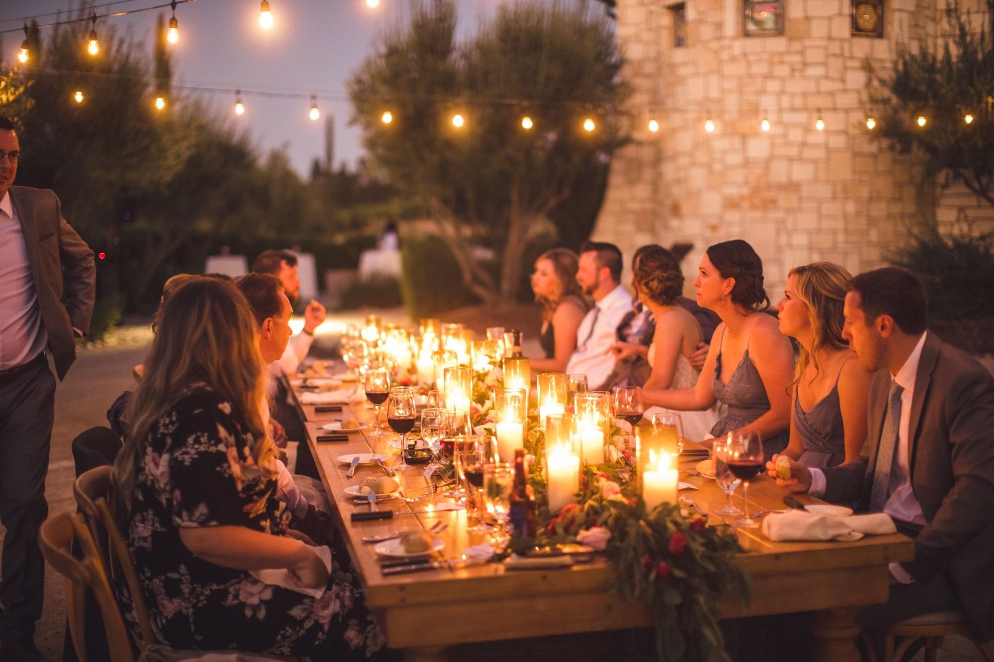 Group of people enjoying a private candlelit dinner in the gardens at dusk