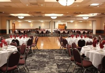 Banquet hall with round tables set by red napkins, maroon chairs surrounding a wood dance floor at The Glenmore Inn
