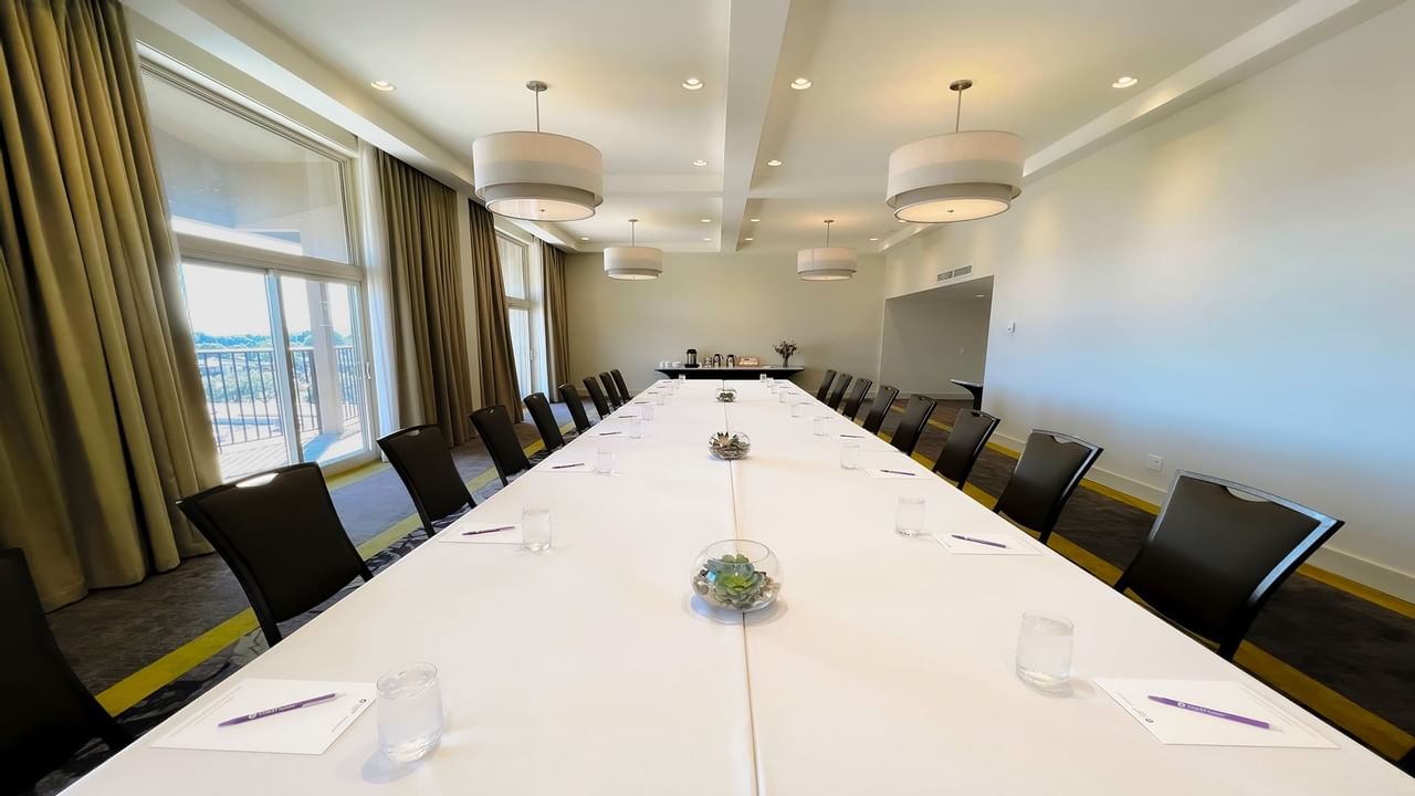 Long boardroom table set with water, pens and chairs