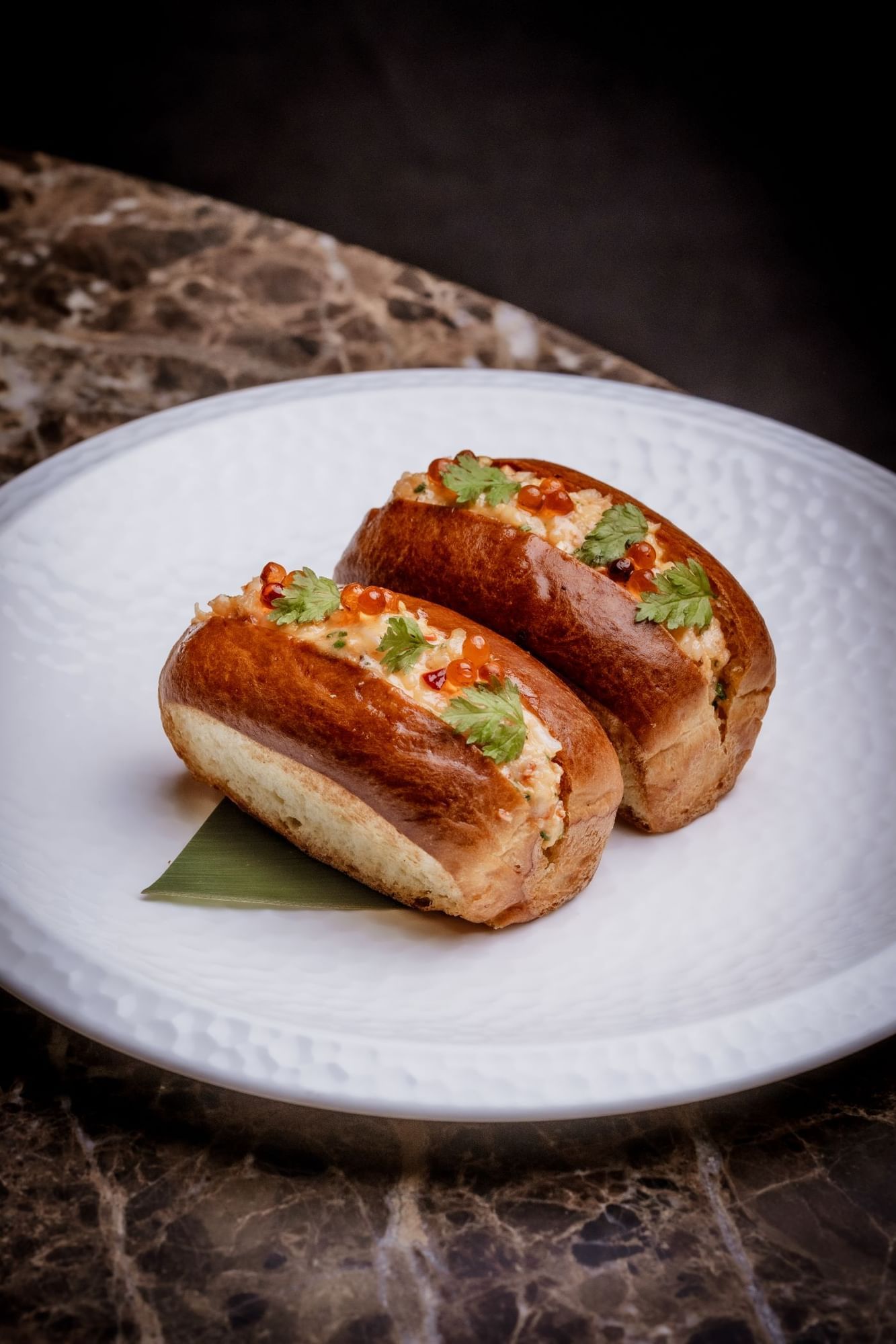 Two stuffed lobster rolls on a white plate with garnishes from the By Night Menu at The May Fair Bar