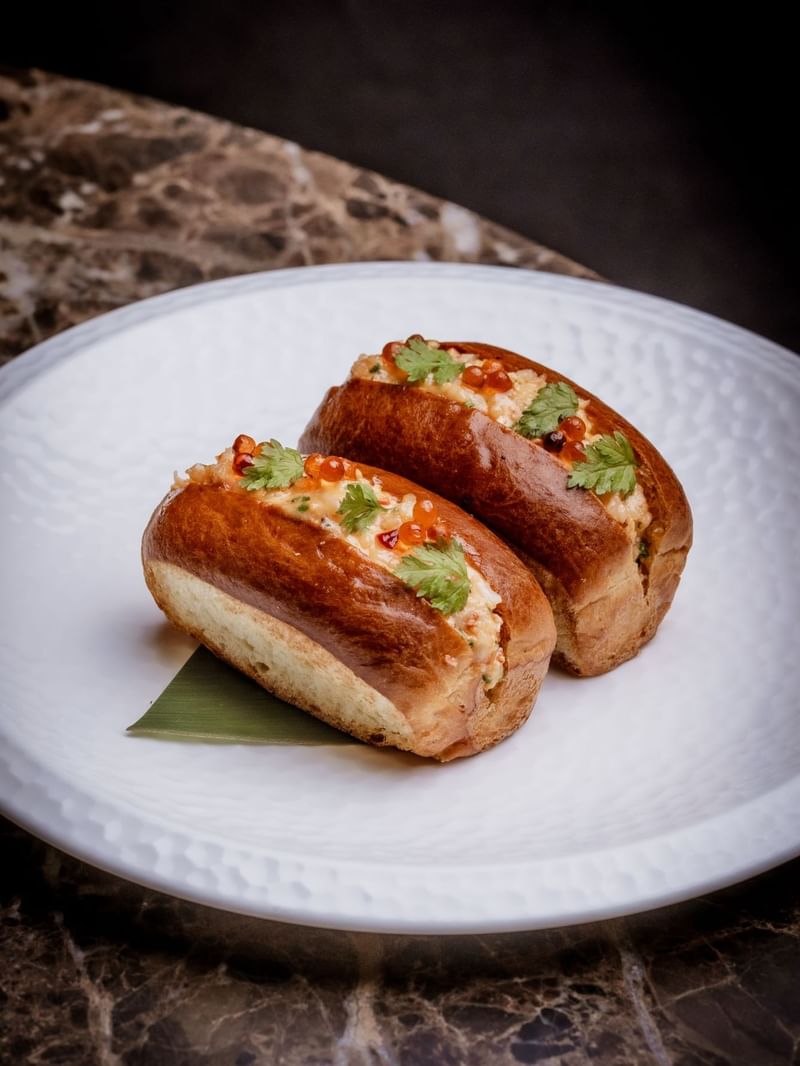 Two stuffed lobster rolls on a white plate with garnishes from the By Night Menu at The May Fair Bar