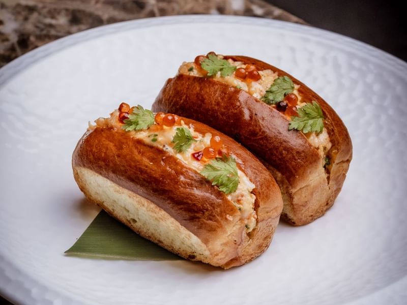 Two stuffed lobster rolls on a white plate with garnishes from the By Night Menu at The May Fair Bar