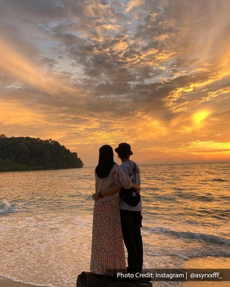 a couple standing on driftwood facing the ocean 