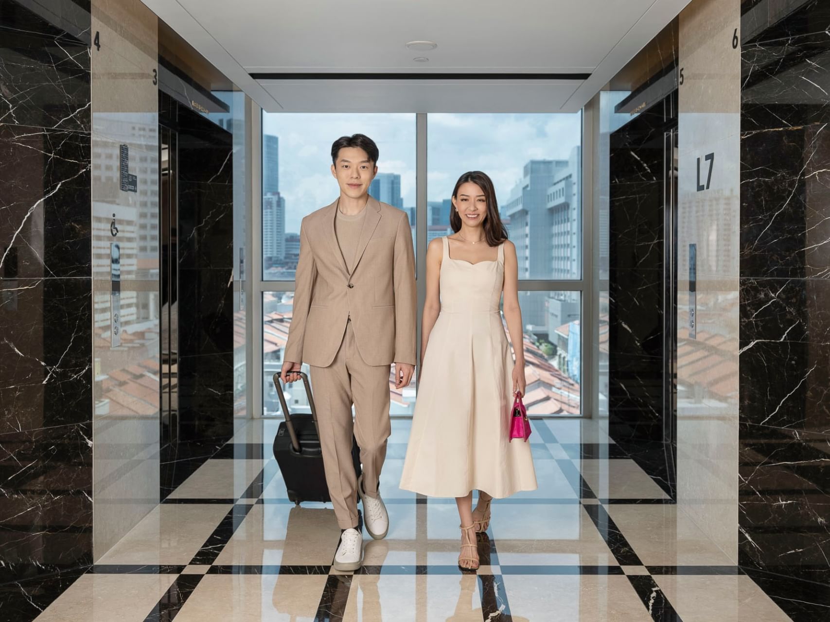 A well-dressed couple walks through a Orchid Hotel Singapore hotel lobby with marble walls and city views beyond the elevators.