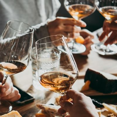 Personen stoßen mit Weingläsern an, auf dem Tisch liegen Käseplatten.