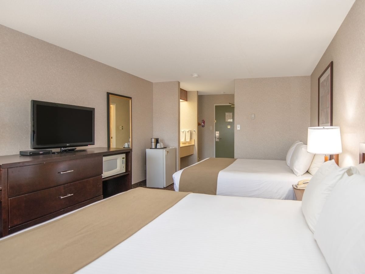 A hotel room with two beds, a TV, dresser, and a bathroom in the background.