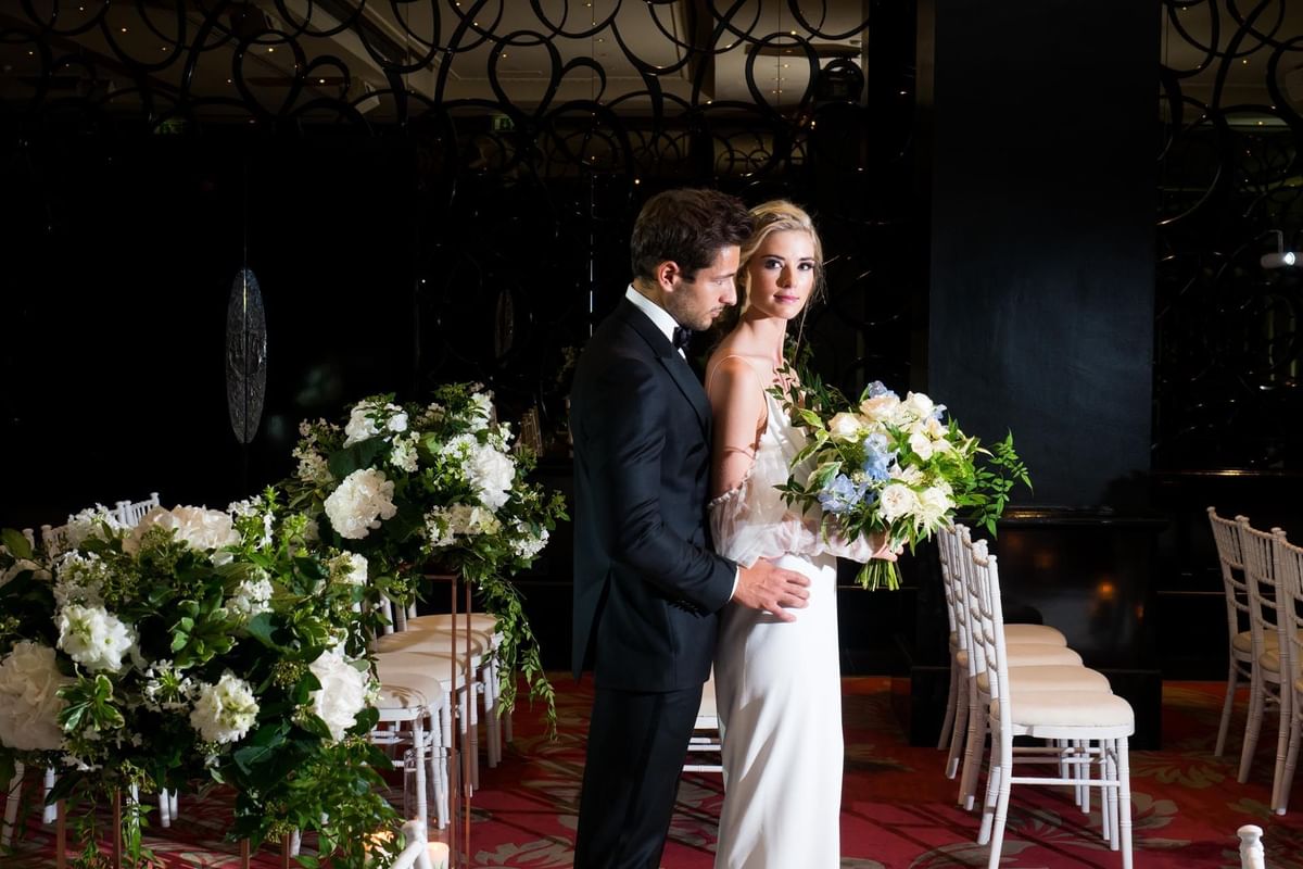 Bride & groom posing in Danziger Suite with beautiful floral arrangements at The May Fair Hotel