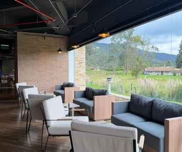 Outdoor covered lounge terrace with modern armchairs and sofas facing green hills and open fields at Hotel B3 Sibelius