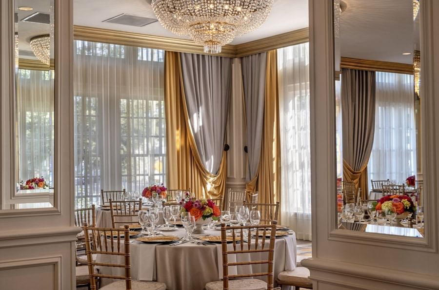 Table with flowers by gold drapes under a crystal chandelier in Crystal Ballroom at Warwick Melrose Dallas