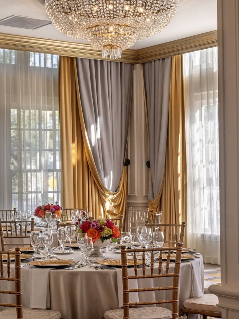 Table with flowers by gold drapes under a crystal chandelier in Crystal Ballroom at Warwick Melrose Dallas