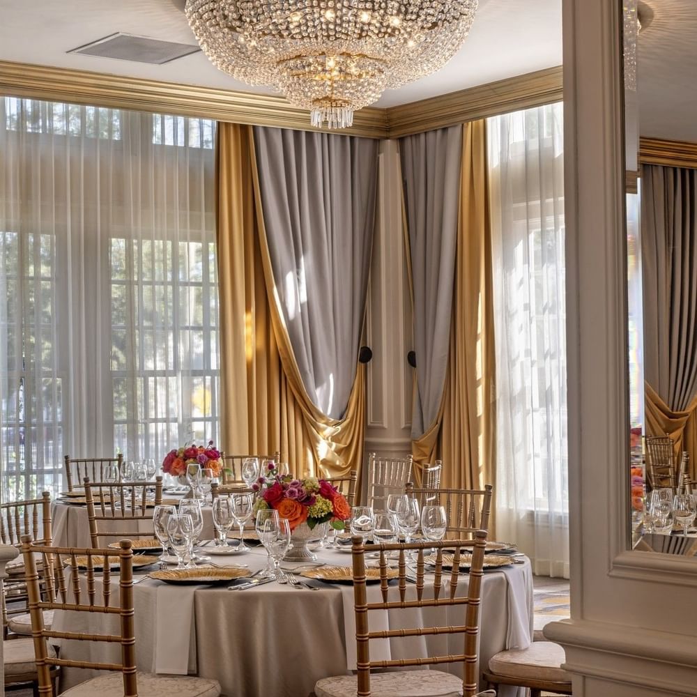 Table with flowers by gold drapes under a crystal chandelier in Crystal Ballroom at Warwick Melrose Dallas