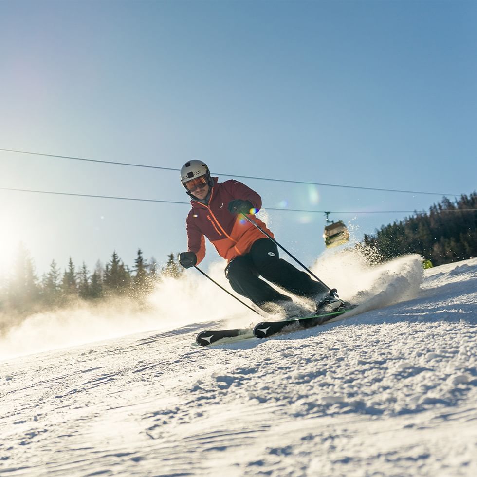 Sciatore in discesa su una pista innevata con sci e bastoncini, sotto un cielo azzurro luminoso.