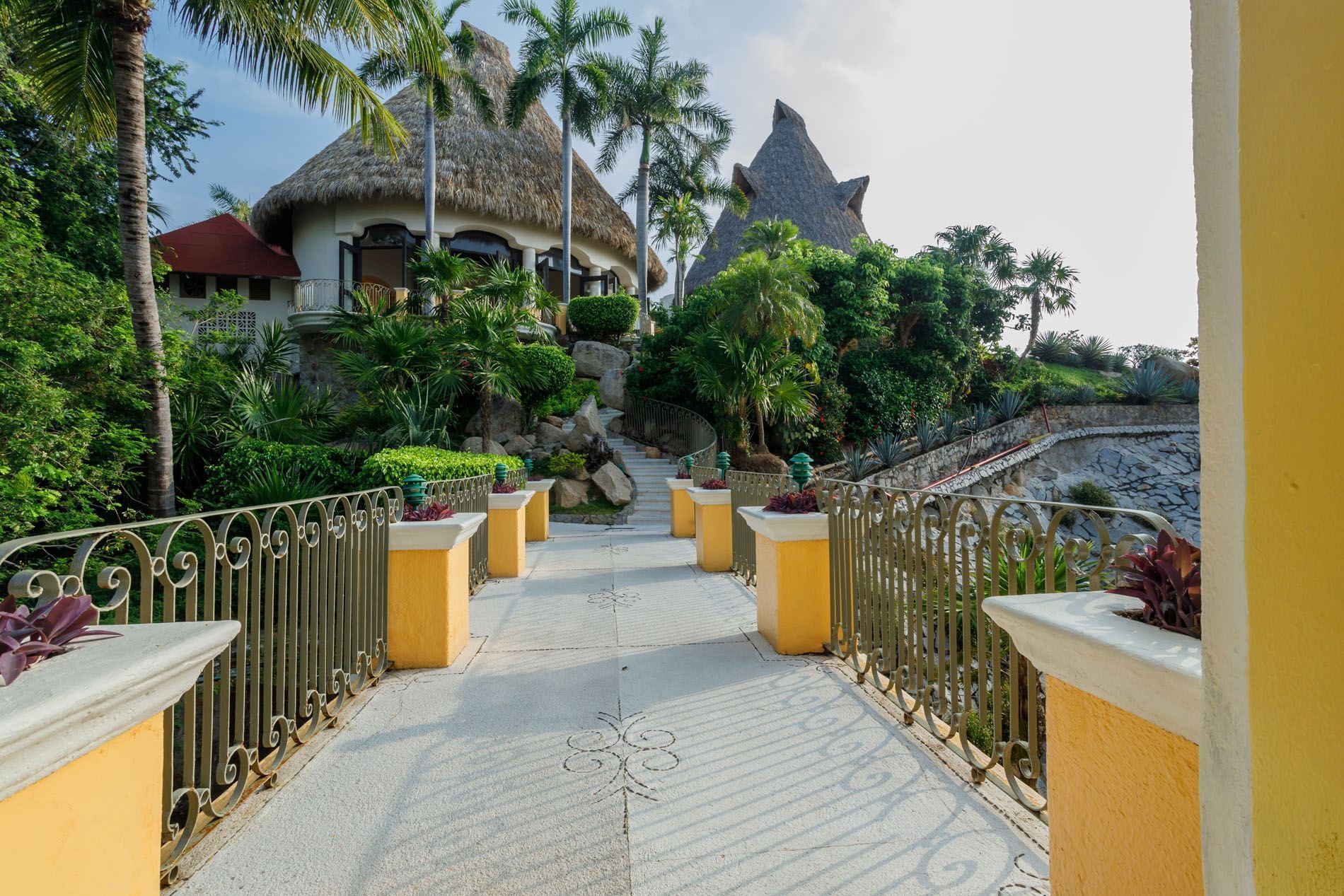 Scenic stone walkway in Maricia Bar lined with yellow pillars and lush tropical greenery at Quinta Real Acapulco